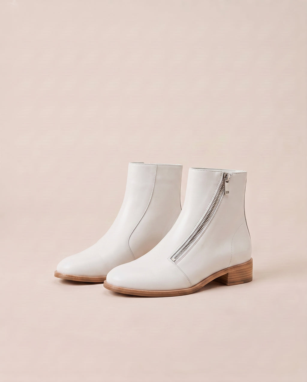 A pair of white ankle boots with a side zipper and a low block heel, displayed on a solid light beige background.