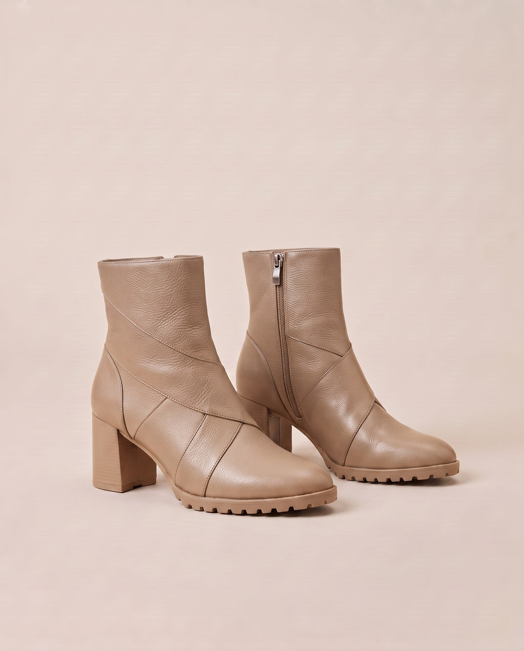 A pair of beige ankle boots with block heels, side zippers, and chunky lug soles, displayed on a solid beige background.