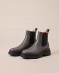 A pair of dark gray Chelsea boots with black elastic side panels and chunky black platform soles, displayed on a warm beige background.
